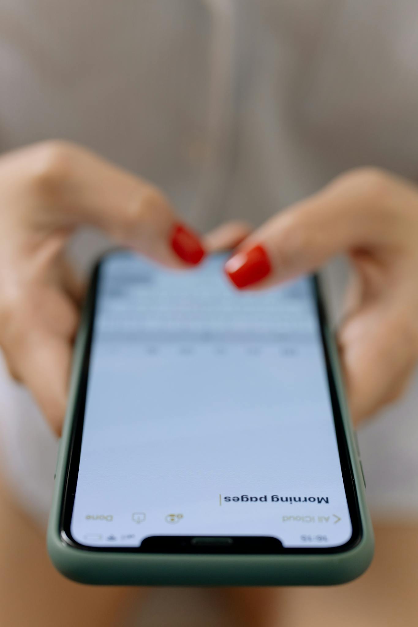 Close-up of a woman's hands with red nails typing on a smartphone indoors.